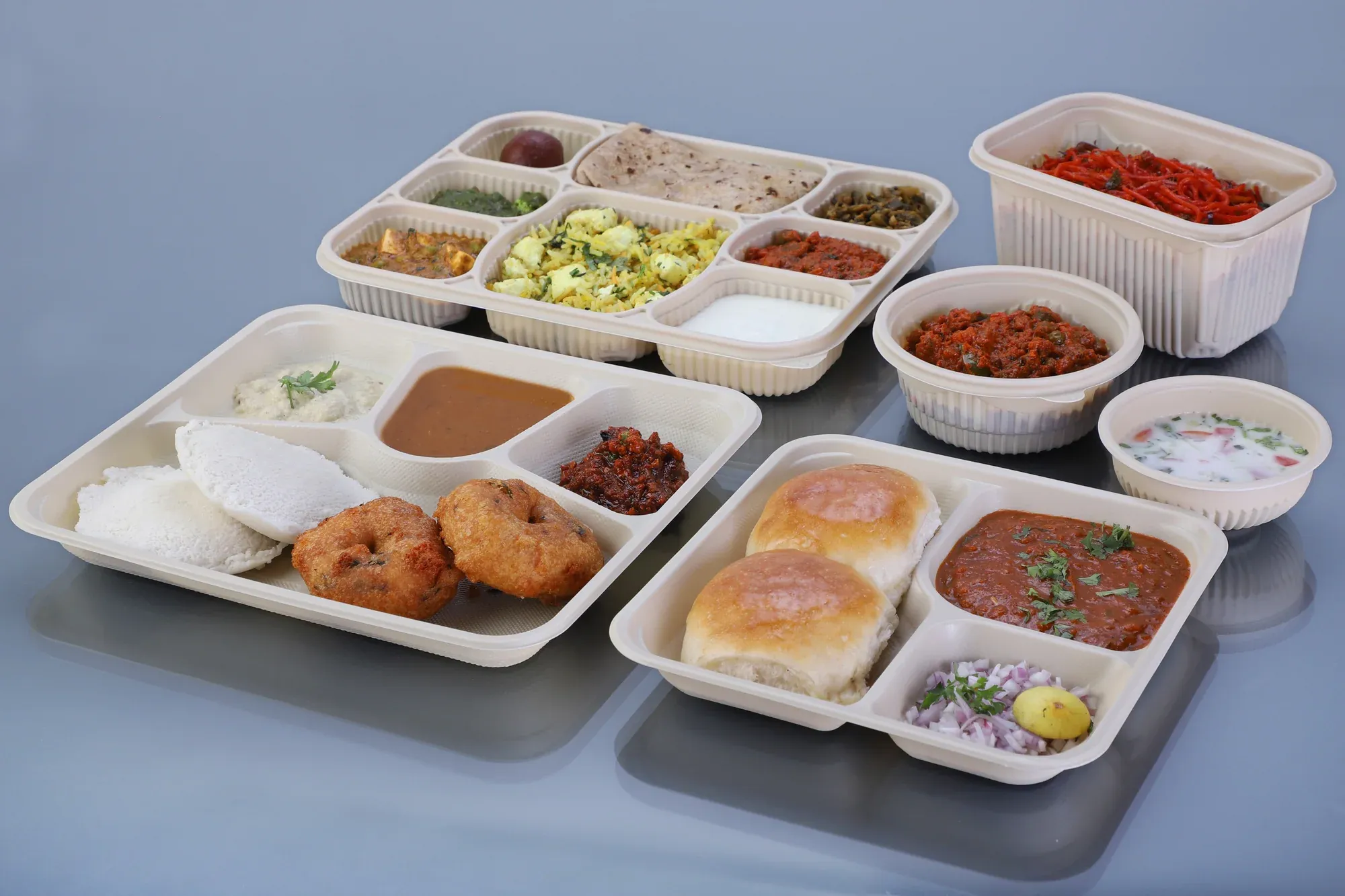 Assorted cornstarch meal trays, bowls and containers filled with Indian foods